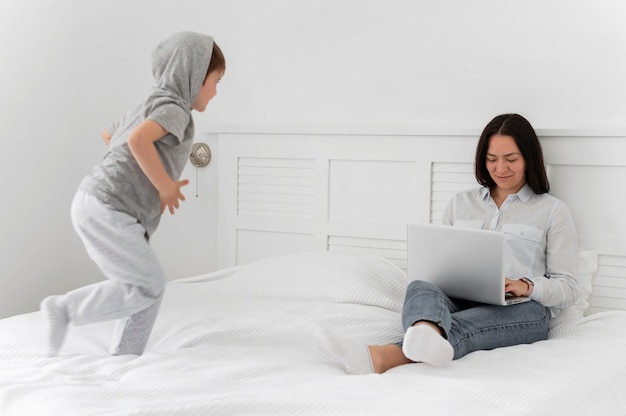 Full shot mother with laptop and kid in bed