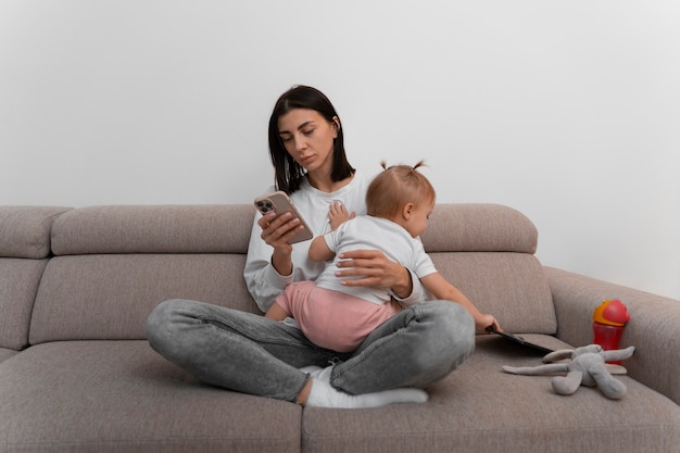 Free photo full shot mother with smartphone and baby