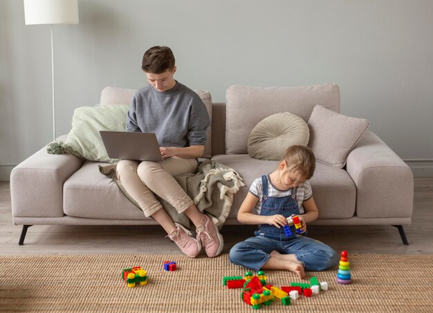 Full shot parent working and kid playing