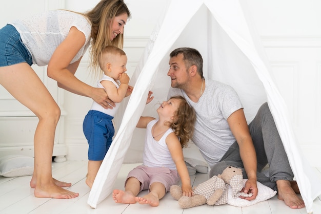 Full shot parents playing with kids with tent