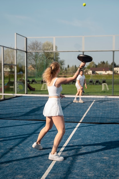 Full shot people playing paddle tennis outside