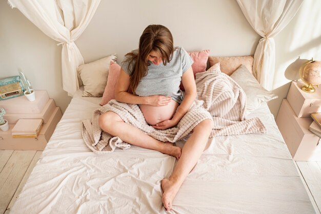 Full shot pregnant woman sitting in bed