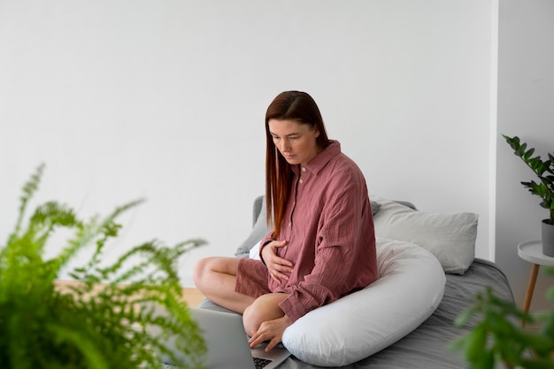 Foto gratuita donna incinta del colpo pieno che si siede a casa