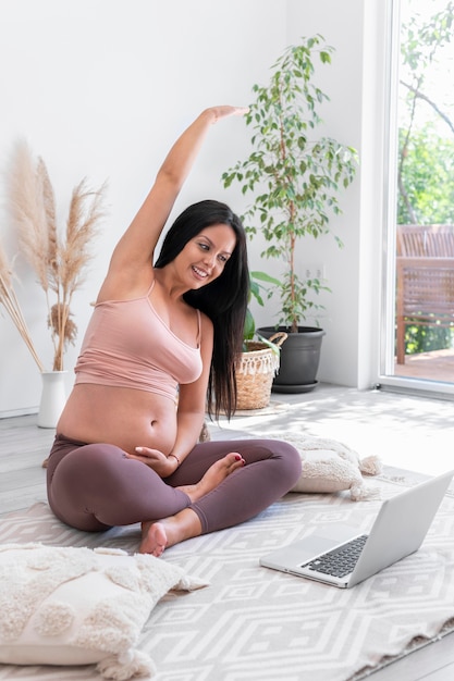 Full shot pregnant woman stretching at home