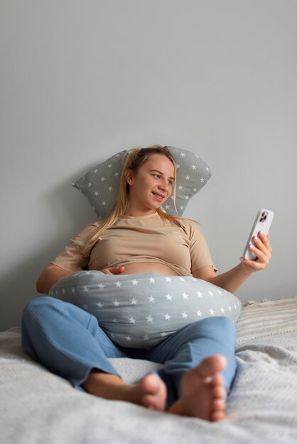 Full shot pregnant woman using nursing pillow