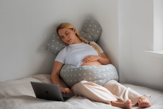 Free photo full shot pregnant woman using nursing pillow