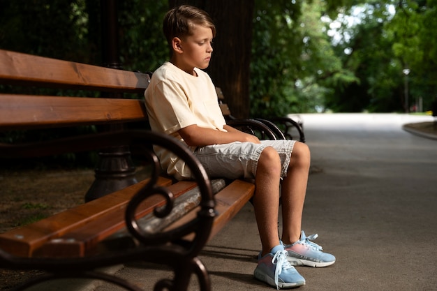 Free photo full shot sad boy sitting on bench