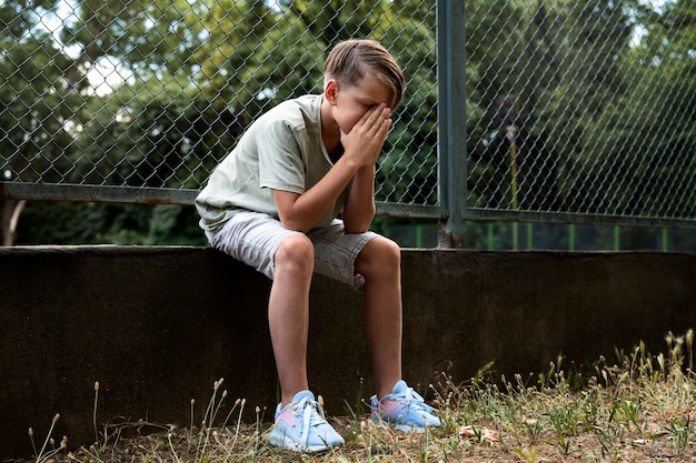 Full shot sad boy sitting outdoors