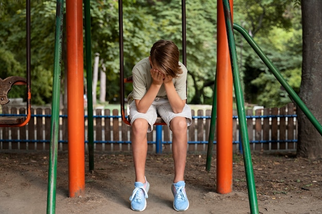 Full shot sad boy sitting on swing