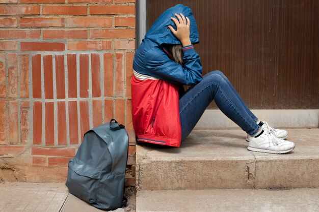 Полный снимок грустной девушки, сидящей на улице