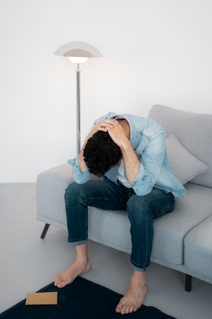 Free photo full shot sad man sitting on couch