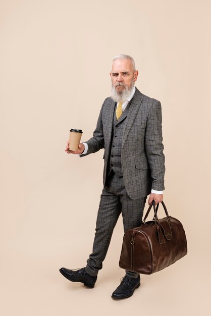 コーヒーカップと荷物を保持しているフルショットの年配の男性