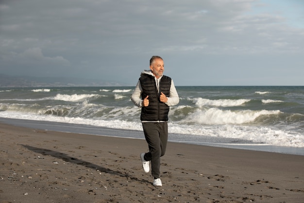 Полный снимок пожилого человека, бегущего по пляжу