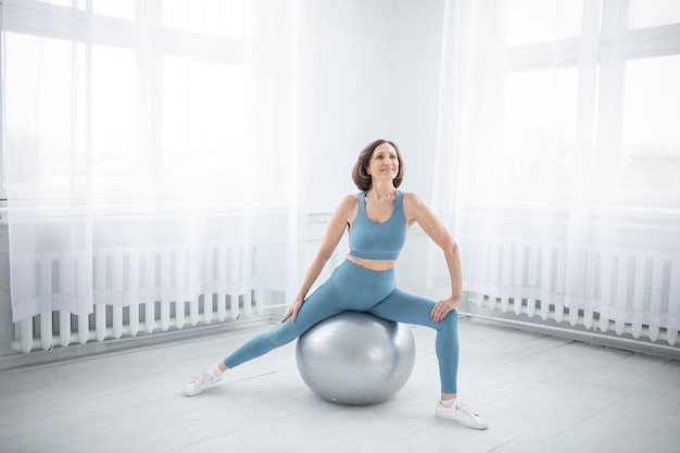 Free photo full shot senior woman training on gym ball