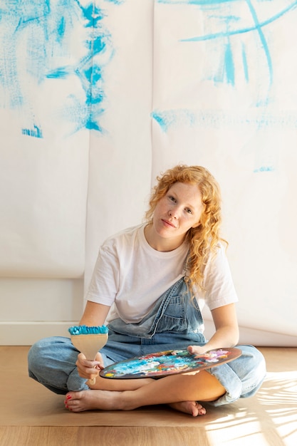 Free photo full shot sitting woman with painting items