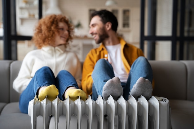 Full shot smiley couple warming up near heater