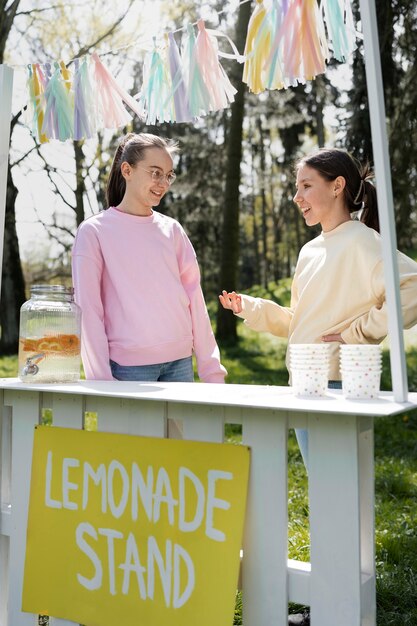 Full shot smiley girls with lemonade stand