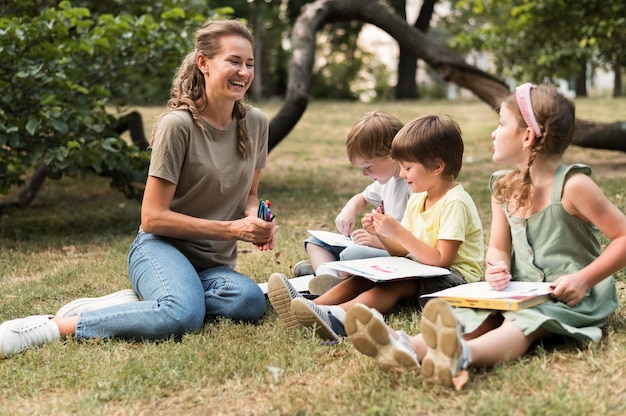 Full shot smiley teacher and kids outdoors