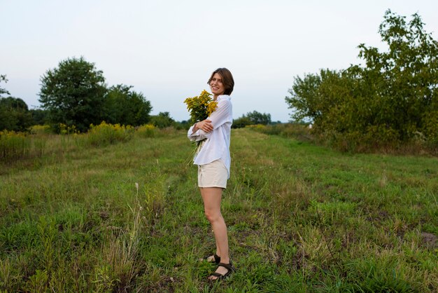 Foto gratuita fiori della holding della donna di smiley del colpo pieno