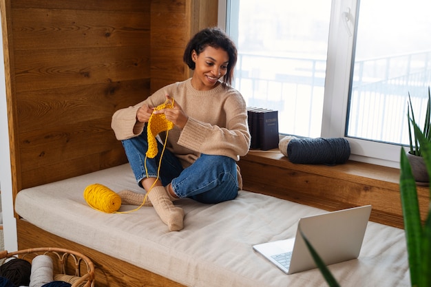 Free photo full shot smiley woman knitting with laptop