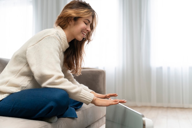 Full shot smiley woman sitting near heater