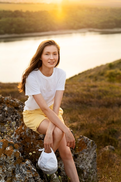 Foto gratuita donna sorridente del colpo pieno che si siede sulla roccia