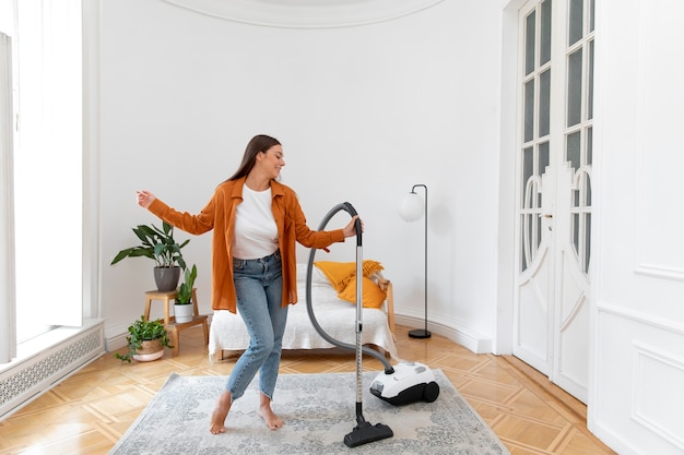 Full shot smiley woman vacuuming carpet