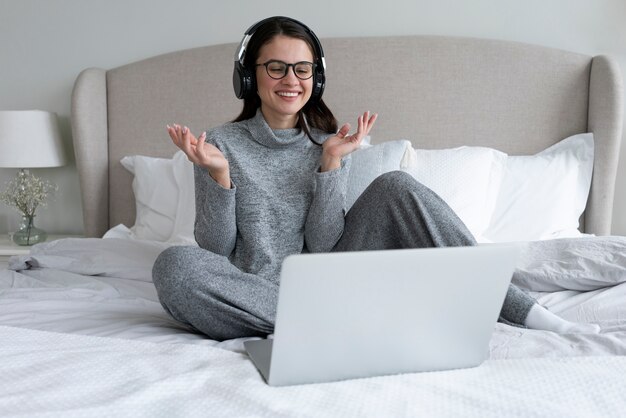 寝室でラップトップを使用して作業しているフルショットの笑顔の女性