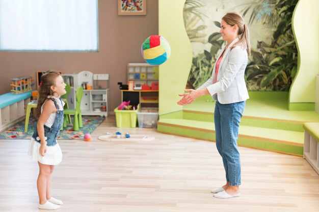 Full shot teacher and girl playing with ball