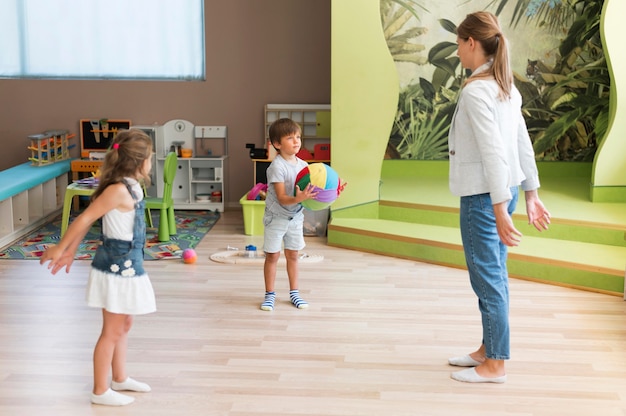 Foto gratuita insegnante di tiro completo e bambini che giocano con la palla