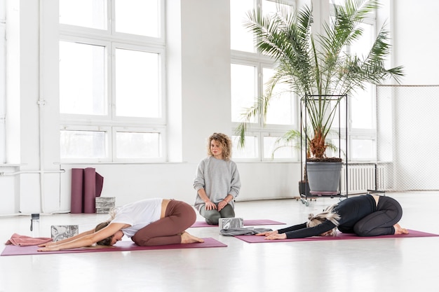 Full shot teacher watching women doing yoga