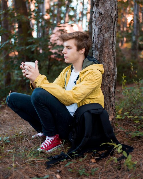 Бесплатное фото Полный выстрел подросток сидит на земле возле дерева