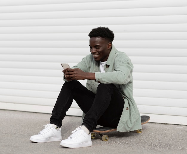 Free photo full shot teen sitting on skateboard outside