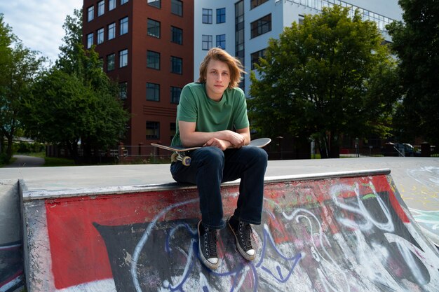 Full shot teen sitting with skateboard