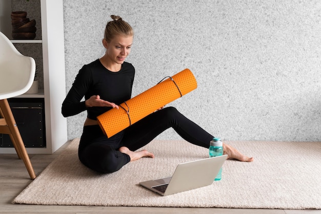 Foto gratuita donna piena del colpo sul tappeto con il computer portatile