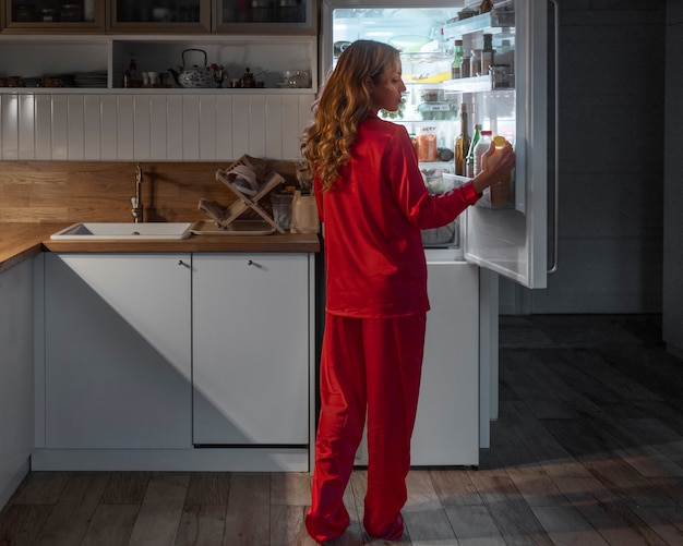 Женщина в полный рост проверяет холодильник ночью