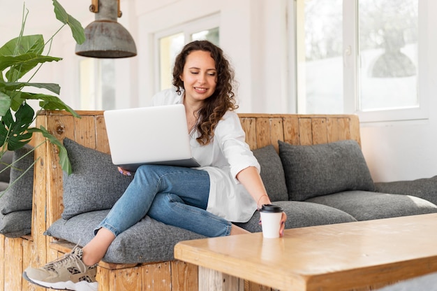 Full shot woman on couch with laptop