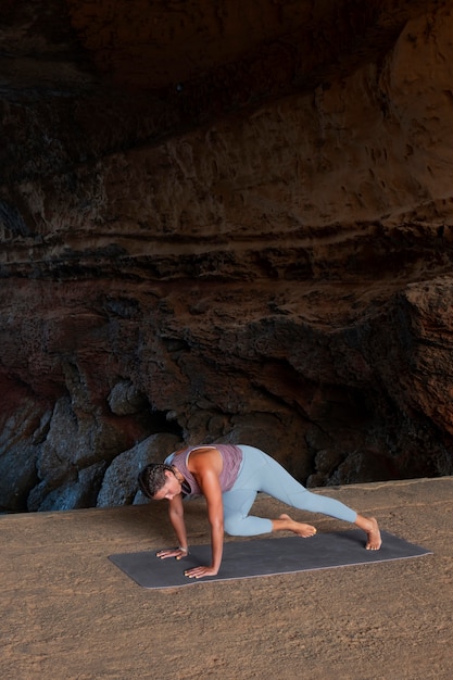 Женщина в полный рост делает позу йоги на коврике