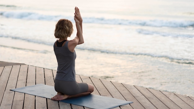 Бесплатное фото Женщина в полный рост делает позу йоги на коврике снаружи