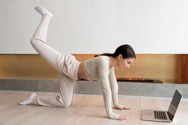 Full shot woman exercising with laptop at home