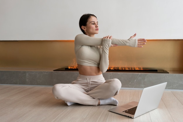 Full shot woman exercising with laptop inside