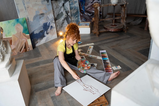 Full shot woman on floor painting with brush