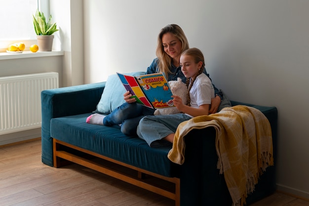 Free photo full shot woman and girl reading comics indoors