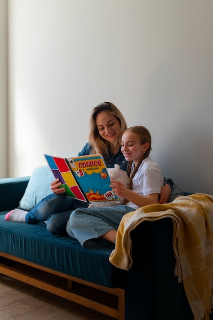 Free photo full shot woman and girl reading comics indoors