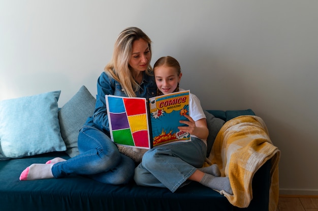 Free photo full shot woman and girl reading comics indoors