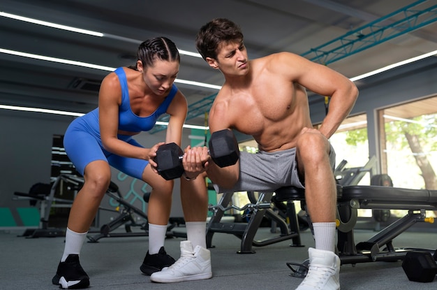 Foto gratuita donna del colpo pieno che aiuta l'uomo in palestra