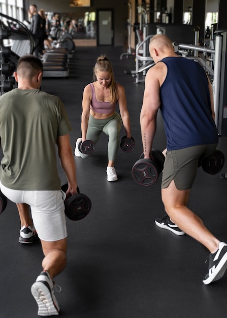 Foto gratuita donna a tutto campo che aiuta gli uomini in palestra