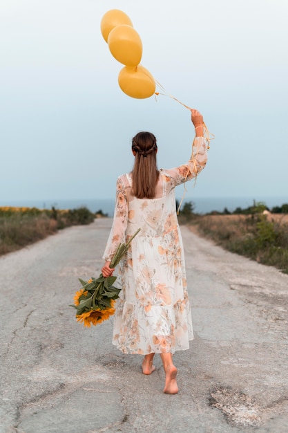 Полный снимок женщина, держащая воздушные шары и цветы