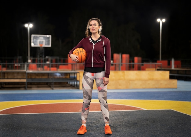 Foto gratuita donna a tutto campo che tiene palla da basket all'esterno