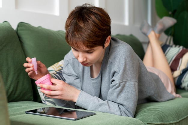 Full shot woman holding menstrual cup on couch